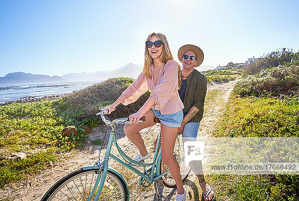 Portrait happy  carefree couple riding bicycle on sunny beach path