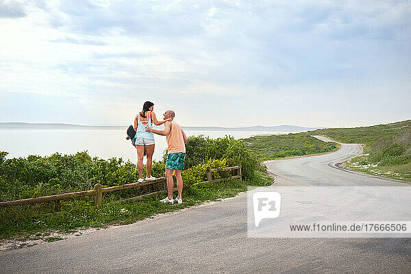 Couple standing on fence at ocean roadside