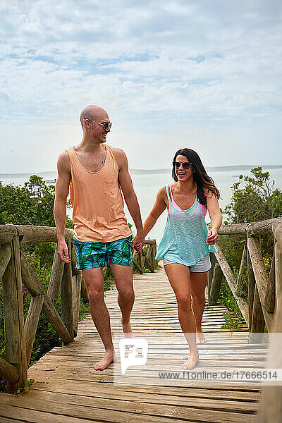 Happy couple holding hands and walking on beach boardwalk
