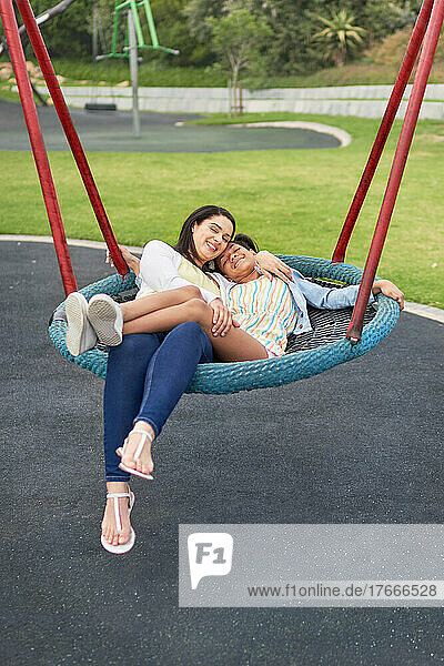 Portrait happy mother and daughter on playground trampoline swing