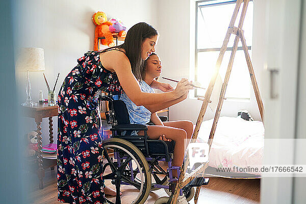 Mother and disabled daughter in wheelchair painting in bedroom