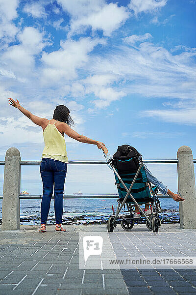 Mother and disabled daughter with arms outstretched on beach boardwalk