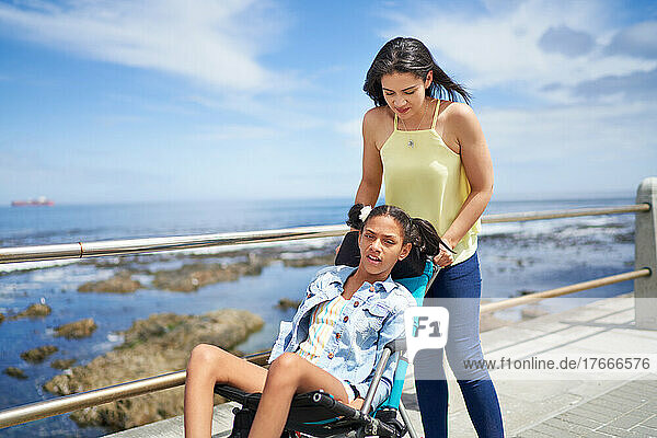 Mother pushing disabled daughter in pushchair on ocean boardwalk