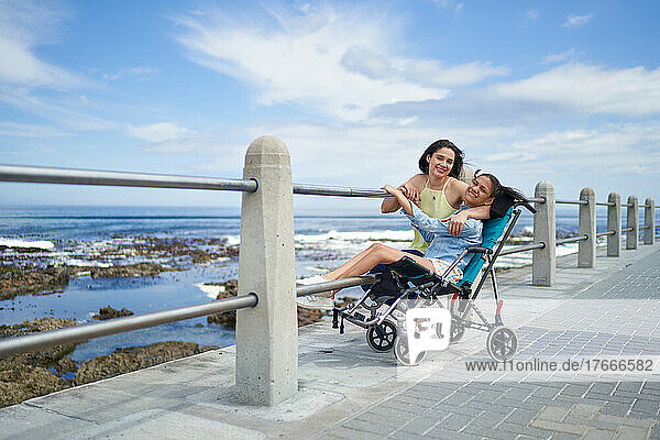 Portrait happy mother and disabled daughter in pushchair at beach