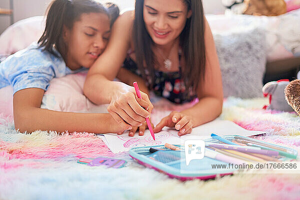 Mother and daughter drawing with marker pen in notebook on rug