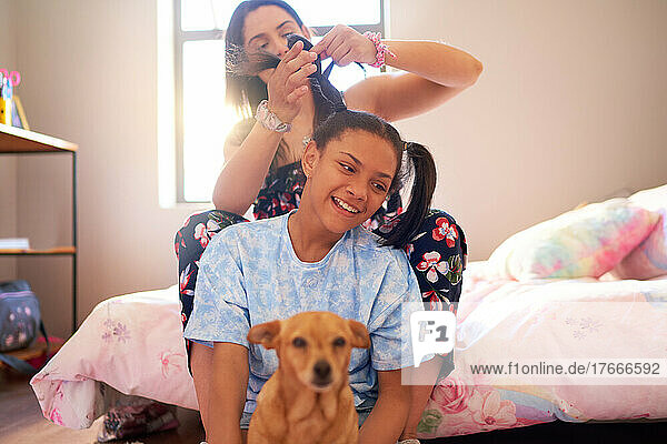 Mother fixing hair for daughter with dog in bedroom