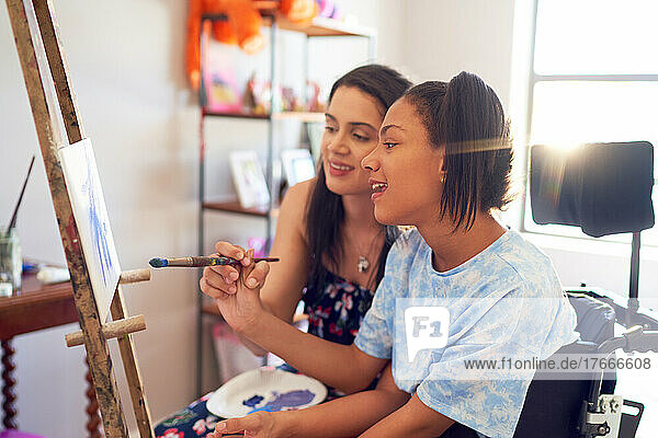 Mother and disabled daughter painting at easel in bedroom