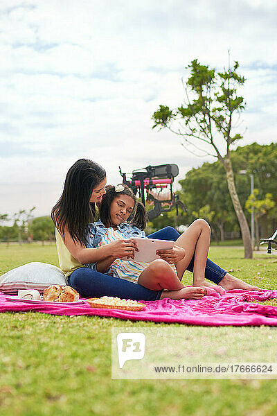 Mother and disabled daughter using digital tablet on blanket in park