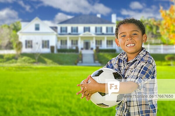 Süßer gemischtrassiger Junge hält Fußball vor einem schönen Haus