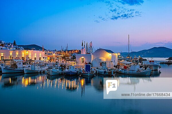 Picturesque view of Naousa town in famous tourist attraction Paros island  Greece with traditional whitewashed houses and moored fishing boats and seaside restaurants and cafe illuminated in night