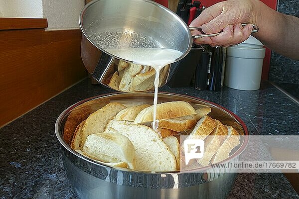 Swabian cuisine  pouring hot milk over sliced bread rolls  preparing simple cherry pudding  poor people's food  using leftovers  dessert from the oven  casserole with stale bread rolls  stale bread  baking  baked goods  cooking pot  man's hand  traditional cuisine  food photography  studio  Germany  Europe