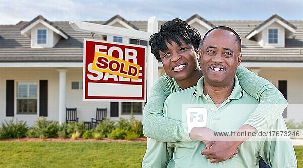 Glückliches afrikanisches amerikanisches Paar vor schönem Haus und zum Verkauf stehendem Immobilienschild