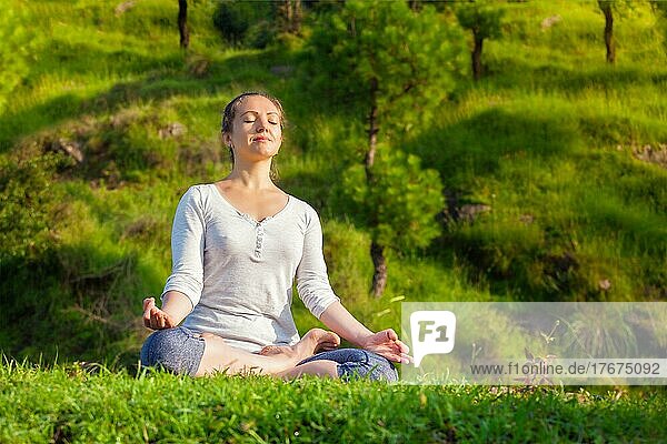 Junge sportliche  fitte Frau macht Yoga im Freien  meditiert und entspannt in Padmasana Lotus Pose mit Kinn Mudra auf grünem Gras im Wald