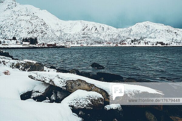 Norwegischer Fjord mit traditionellen roten Rorbu-Häusern am Fjordufer im Schnee im Winter. Lofoten Inseln  Norwegen  Europa