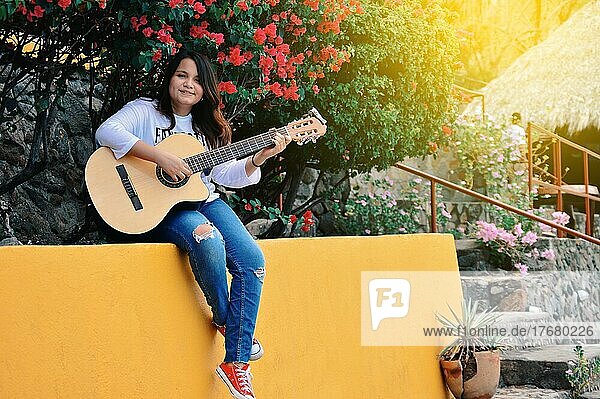 Pretty smiling girl sitting playing guitar outdoors  Portrait of smiling girl playing guitar  Lifestyle of girl playing guitar outdoors