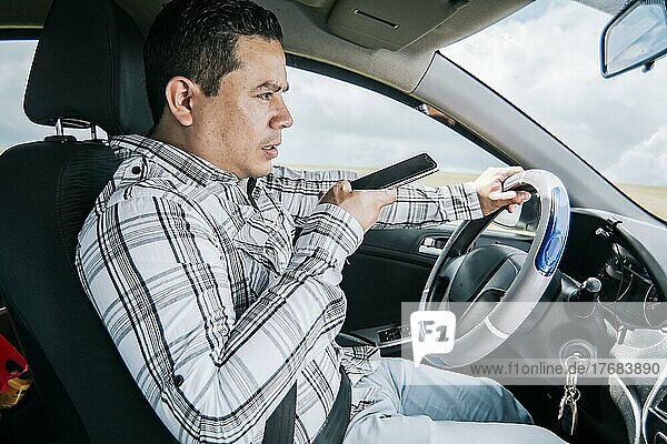 Man in his car sending voice notes with his cell phone  Side view of a young man sitting inside the car talking on the phone while driving  Young man sitting in the car talking on the phone while driving