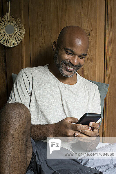 Man using smart phone while sitting in bedroom