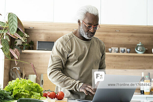 Senior man watching recipe on laptop in kitchen