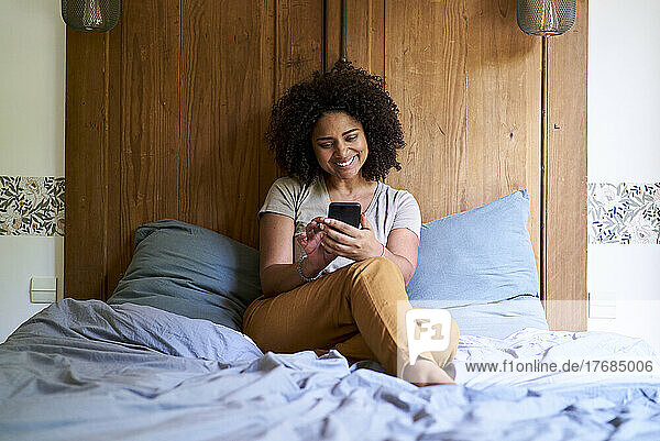 Woman using smart phone while sitting in bedroom