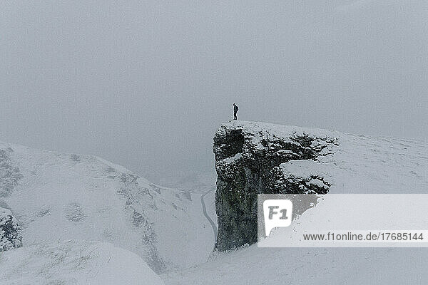 Man standing at edge of mountain rock in snow covered landscape  Winnats Pass  Castleton  England