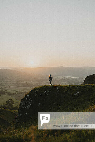Silhouetted female hiker on hilltop overlooking tranquil landscape at sunrise  England