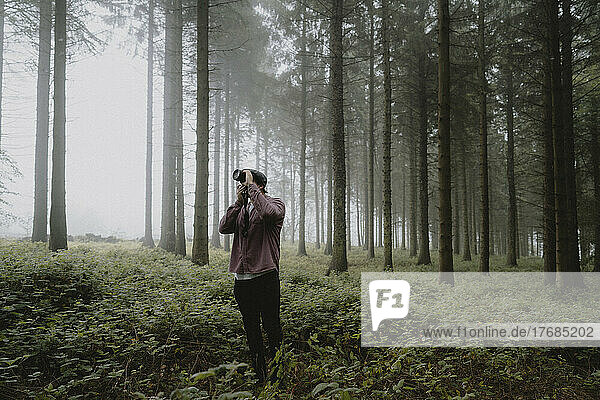 Male photographer with SLR camera in foggy forest with trees  Strines  Derbyshire  England