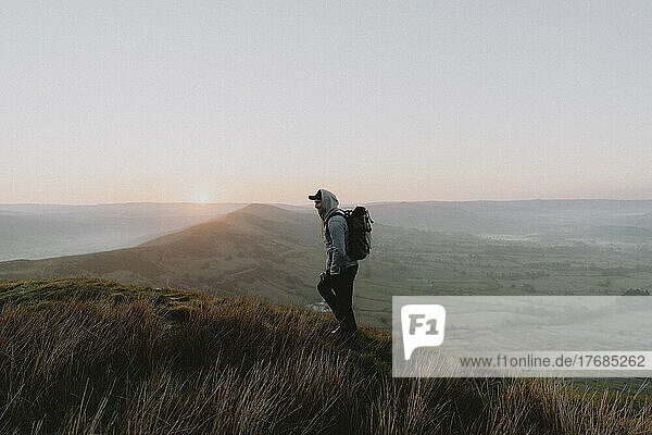 Male hiker with backpack on hill overlooking rural landscape at sunrise  Castleton  England