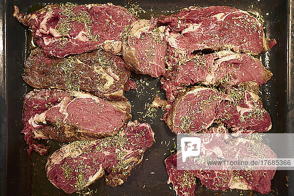 View from above raw steaks with seasoning herbs marinating in tray