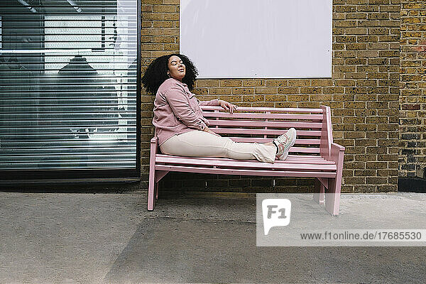 Young woman with eyes closed sitting on pink bench