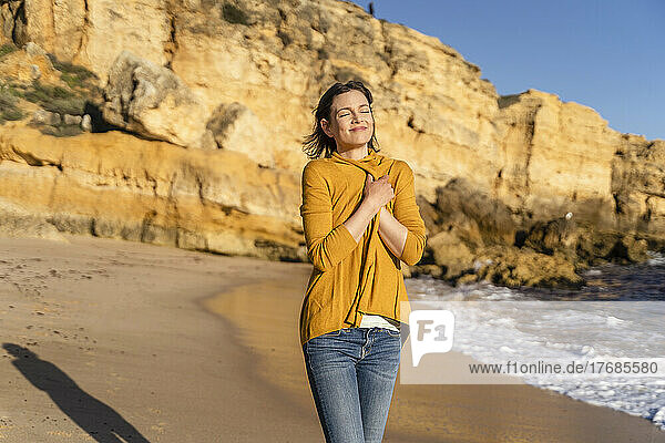 Smiling woman wearing shrug standing in front of rock formation on shore at beach