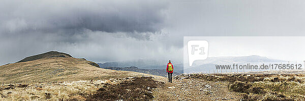 Active senior woman with backpack hiking on mountain under cloudy sky