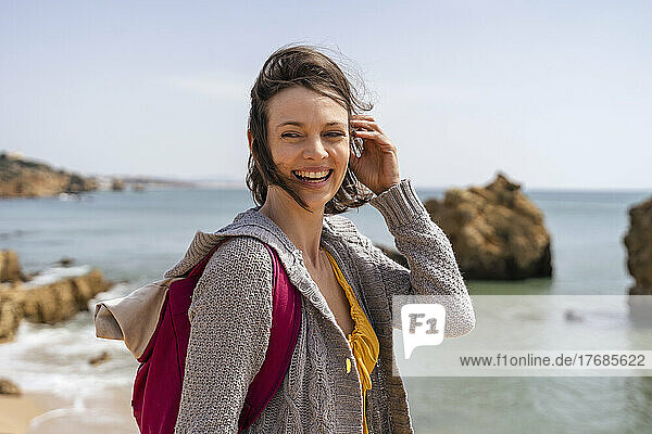 Happy woman wearing backpack standing with hand in hair