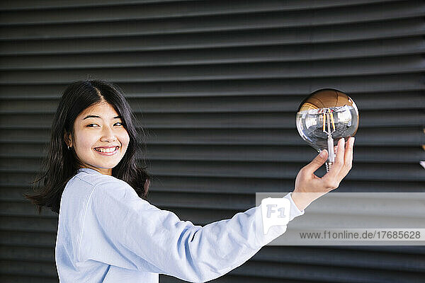 Happy young woman with light bulb by corrugated iron shutter