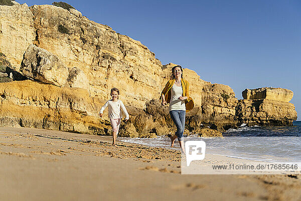 Smiling mother and daughter running on shore at beach