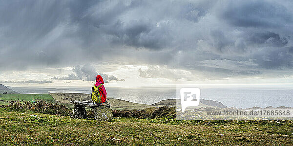 Woman with backpack sitting on bench under cloudy sky