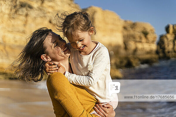 Lächelnde Frau verbringt an einem sonnigen Tag ihre Freizeit mit ihrer Tochter am Strand