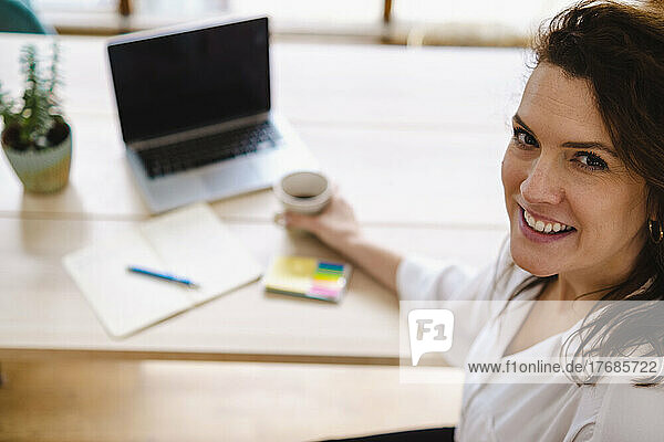 Happy freelancer with laptop sitting at table at home