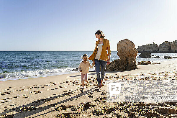 Mother with daughter walking on shore at beach