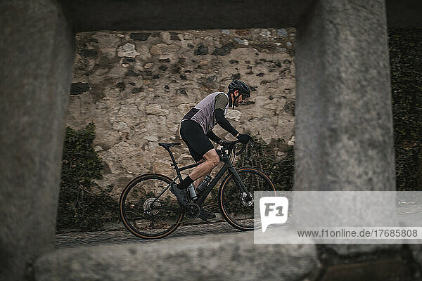 Radfahrer fährt Fahrrad vor Steinmauer