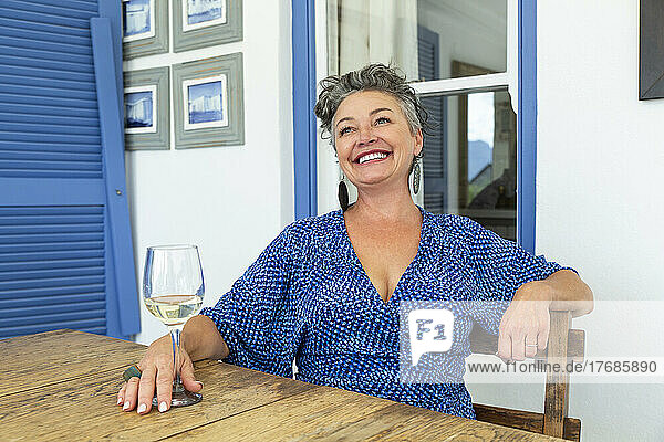 Happy mature woman with glass of wine sitting at table