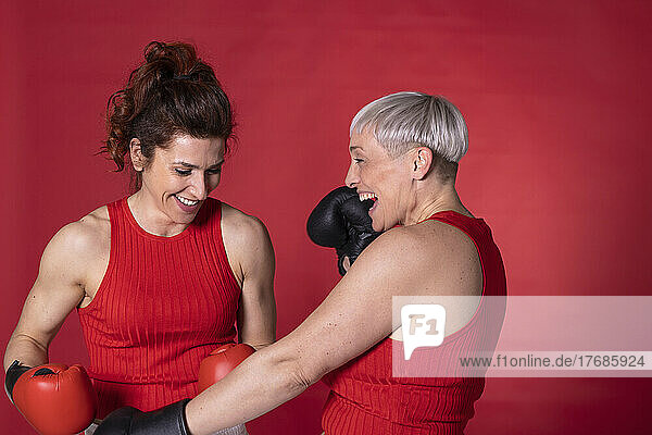 Happy friends with boxing gloves standing against red background