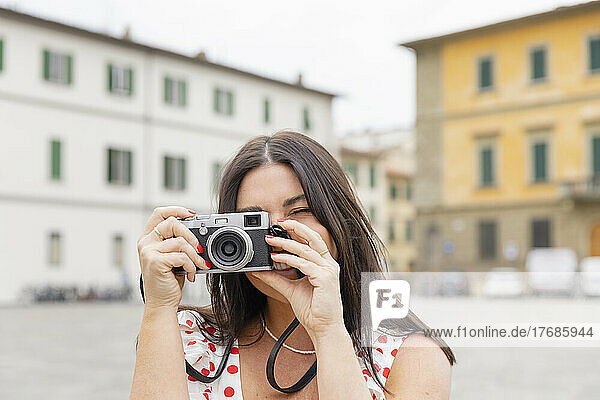 Happy woman taking picture through camera in front of buildings