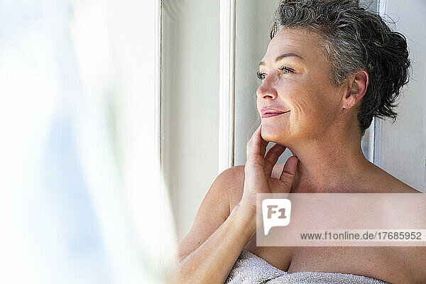 Smiling mature woman standing by window at home