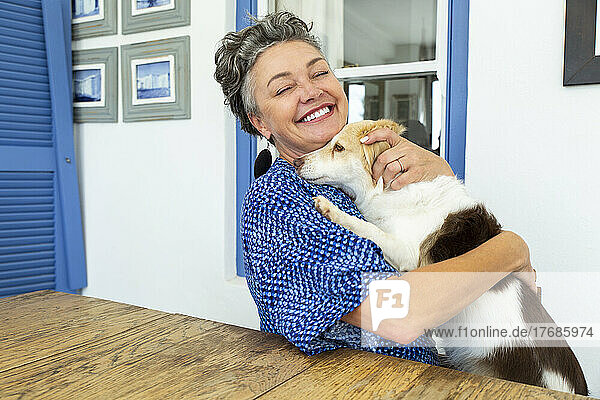Happy mature woman embracing dog sitting at table