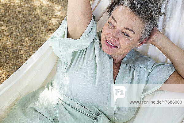 Happy woman with hand behind head lying on hammock