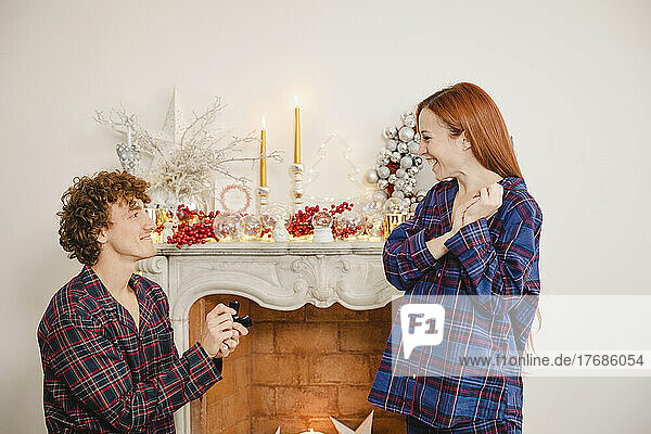 Smiling young man proposing girlfriend in front of marble fireplace