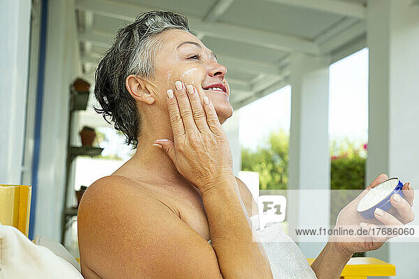 Lächelnde reife Frau  die zu Hause Feuchtigkeitscreme auf das Gesicht aufträgt