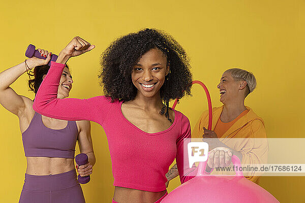 Smiling woman flexing muscles standing with friends against yellow background