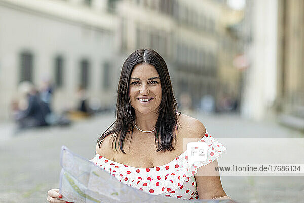 Lächelnde Frau mit langen Haaren hält eine Karte in der Stadt in der Hand