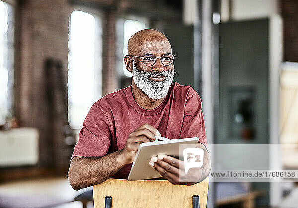 Smiling man with tablet PC contemplating on chair at home